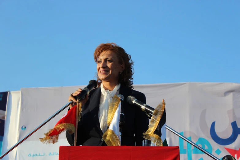 a woman wearing a coat speaking at a podium