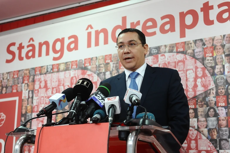 an asian man standing behind a large red podium in front of microphones