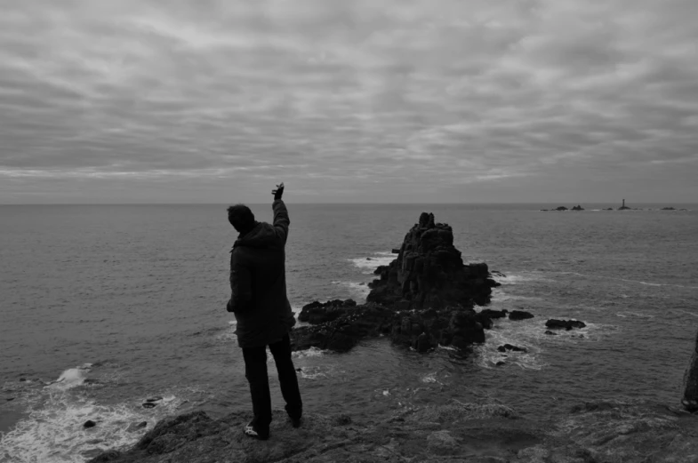 black and white pograph of man on the edge of cliff pointing towards the ocean