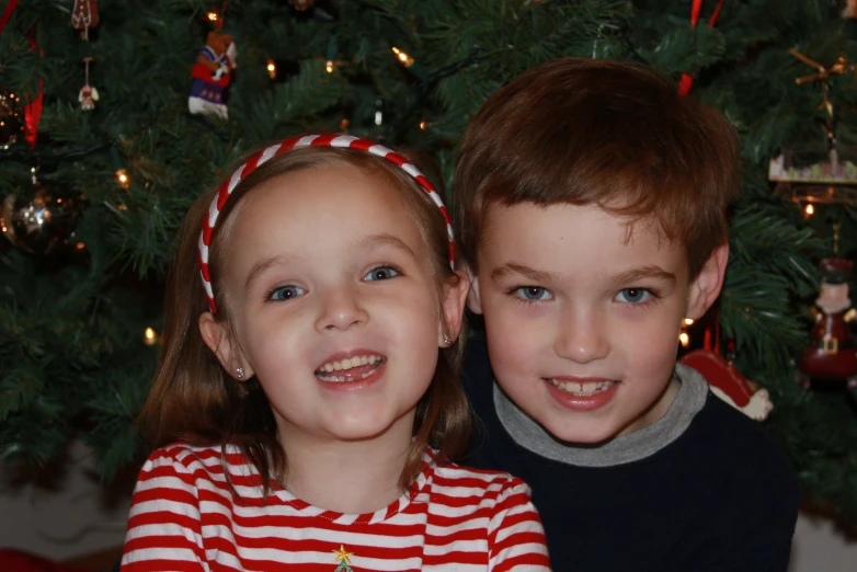 two young children pose together in front of a christmas tree