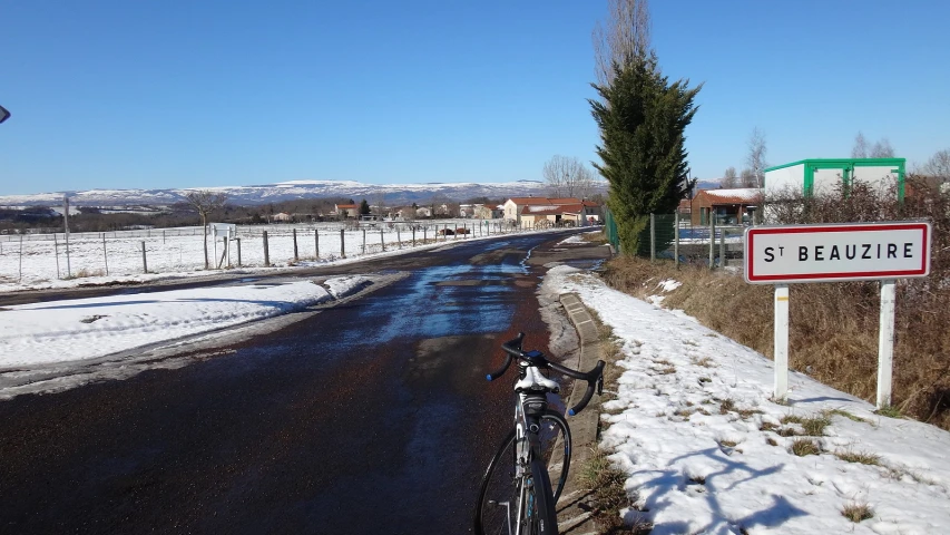 a snowy road with a sign and bicycle leaning up against it