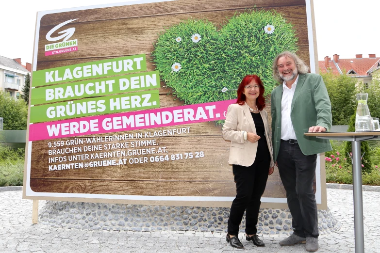 two people standing next to a large sign that says klageenfurst uch dem grunes merz