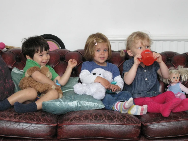 three s sitting on a coach holding teddy bears