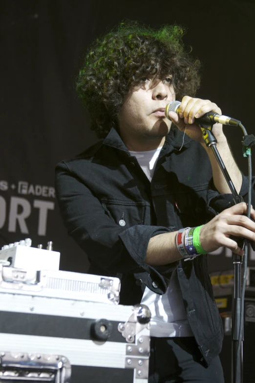 a young man with green hair, wearing a black shirt, standing in front of a microphone