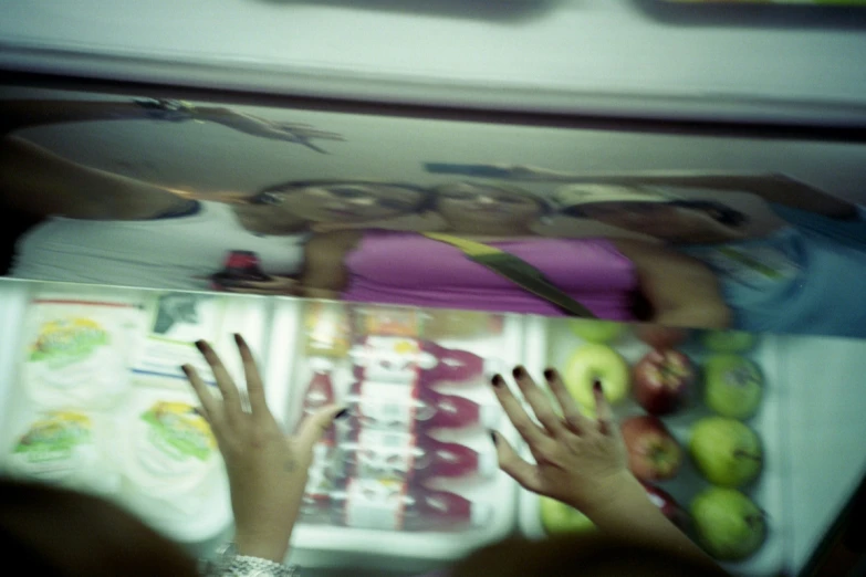 two women are hiding behind a refrigerator with food