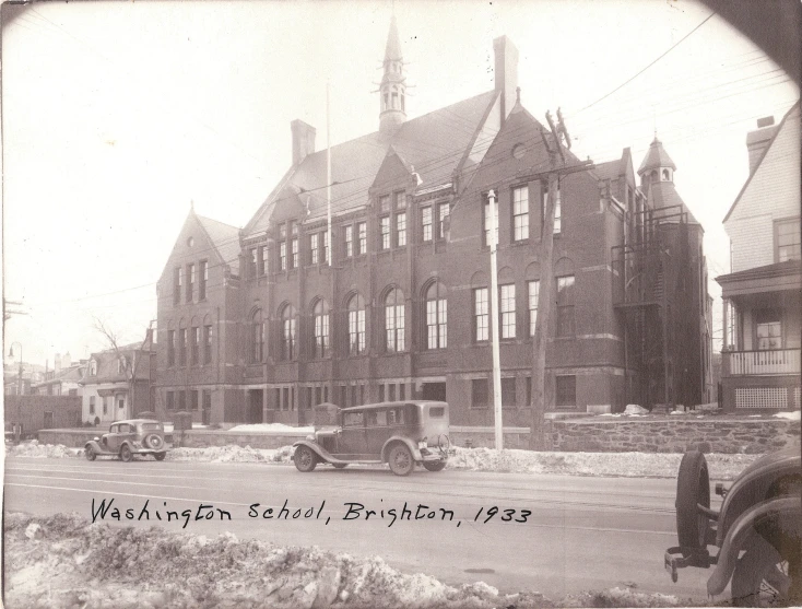 this vintage po shows the view of a school, cars, and buildings