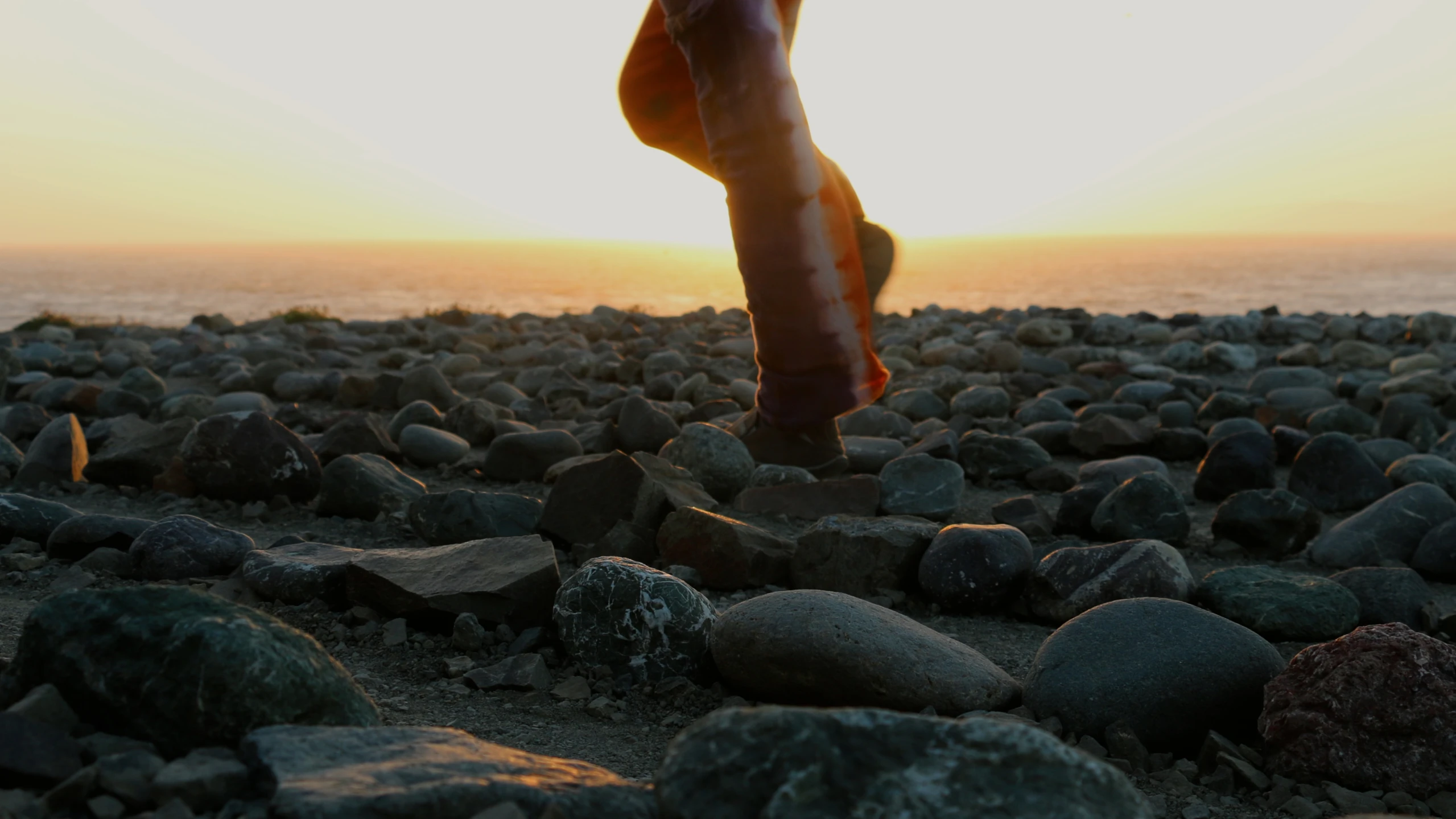 a person standing on rocks is silhouetted against the sun