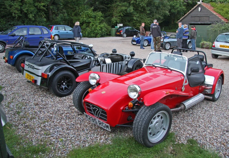 two men look on as a red car sits in the gravel