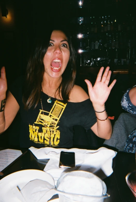 a woman with her mouth open and hands open sitting at a table