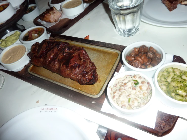 a wooden platter of meat and other foods sit on a table