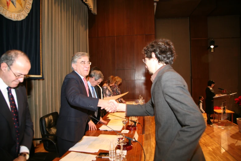 two men shaking hands over paperwork in a courtroom