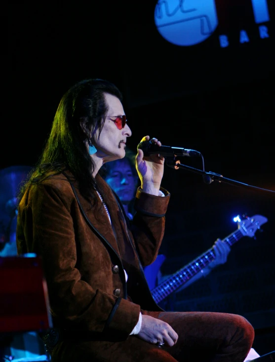 a man sitting down holding a microphone and singing into it