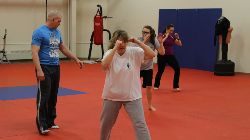 a group of people on a gym floor, wearing boxing gloves