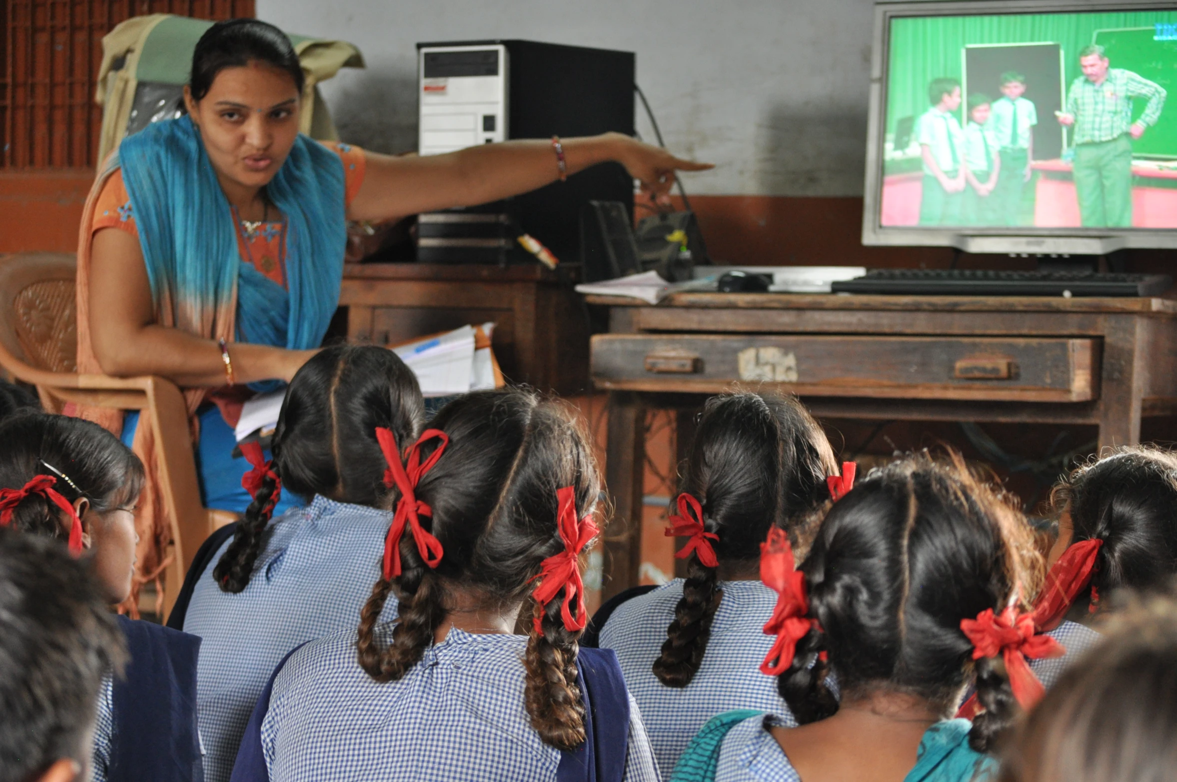 an indian teacher watches a group of children play a game on the television