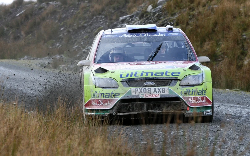 a green car in the dirt near a hill