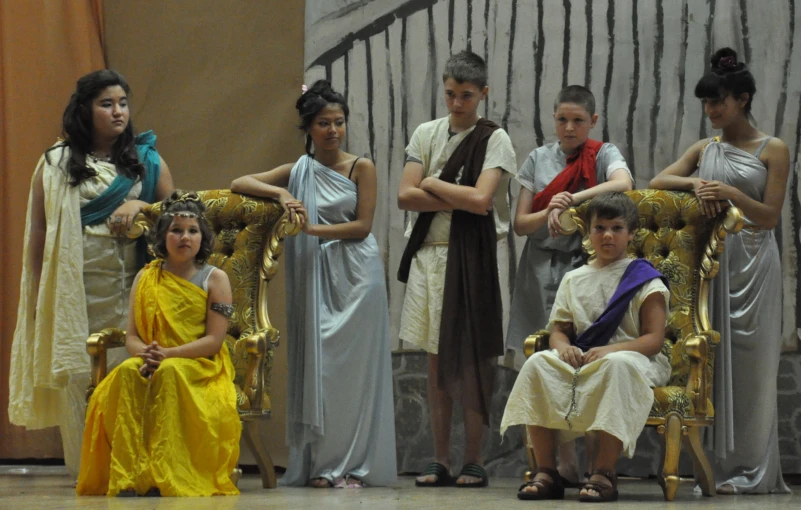 children, adults and young men are sitting on ancient chairs