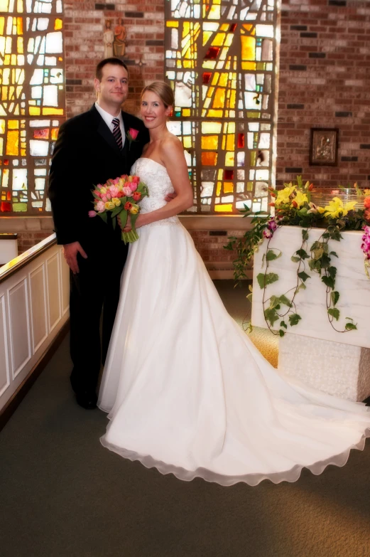 the newly married couple stands in front of the stained glass window