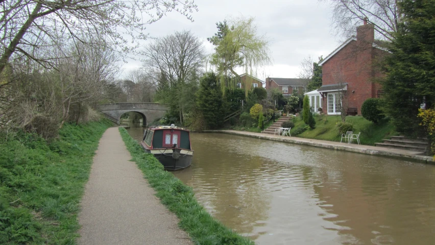 a canal with a boat going down it with green grass on either side and brick buildings in the background