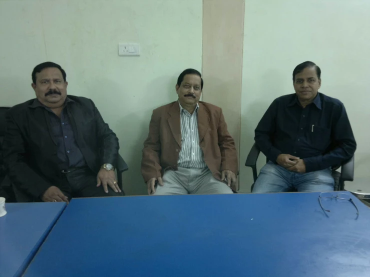 three men sitting down at a blue table