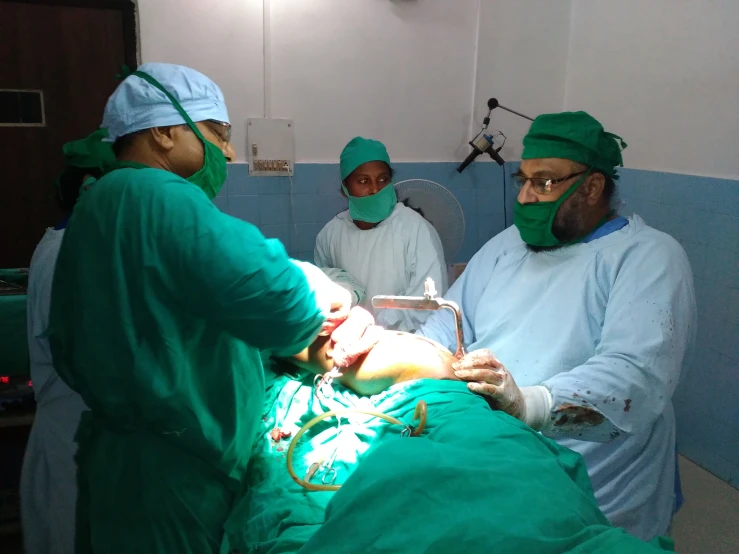 surgical personnel performing  on a person in a green uniform
