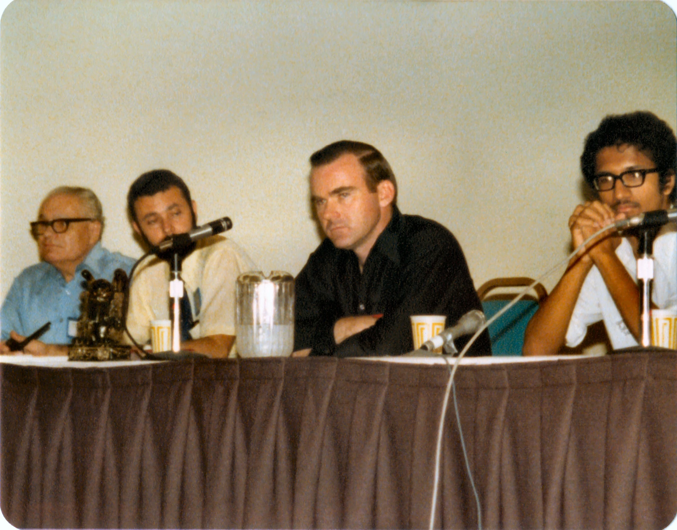 five men sitting at a table with microphones