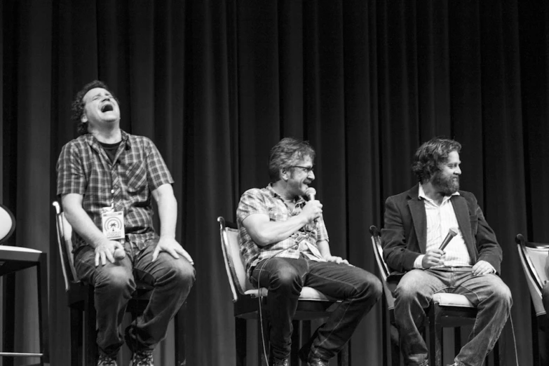 the three men are sitting on chairs at the microphone