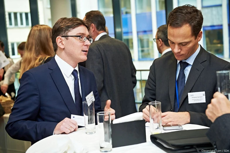 two men sitting at a table in suits talking and talking