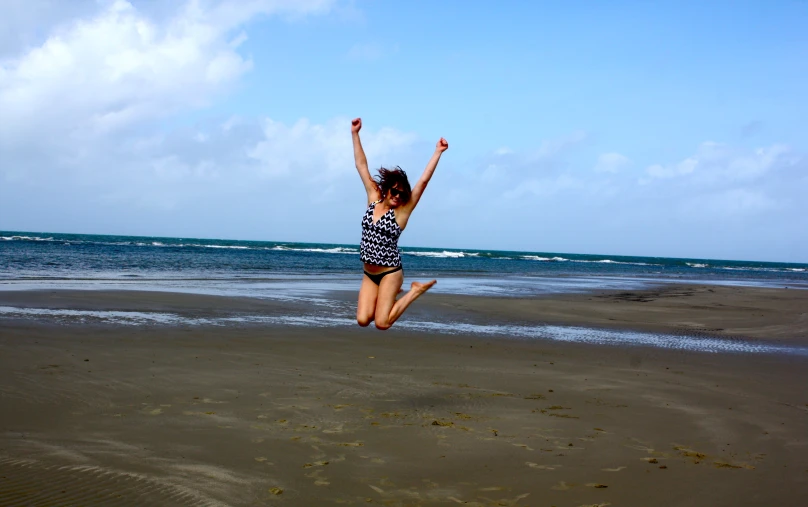 a girl jumping up and down at the beach
