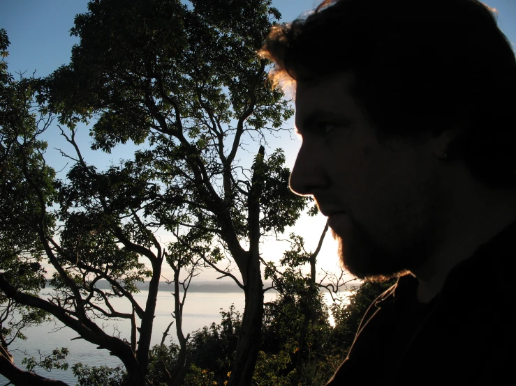 a man standing near some trees in front of water