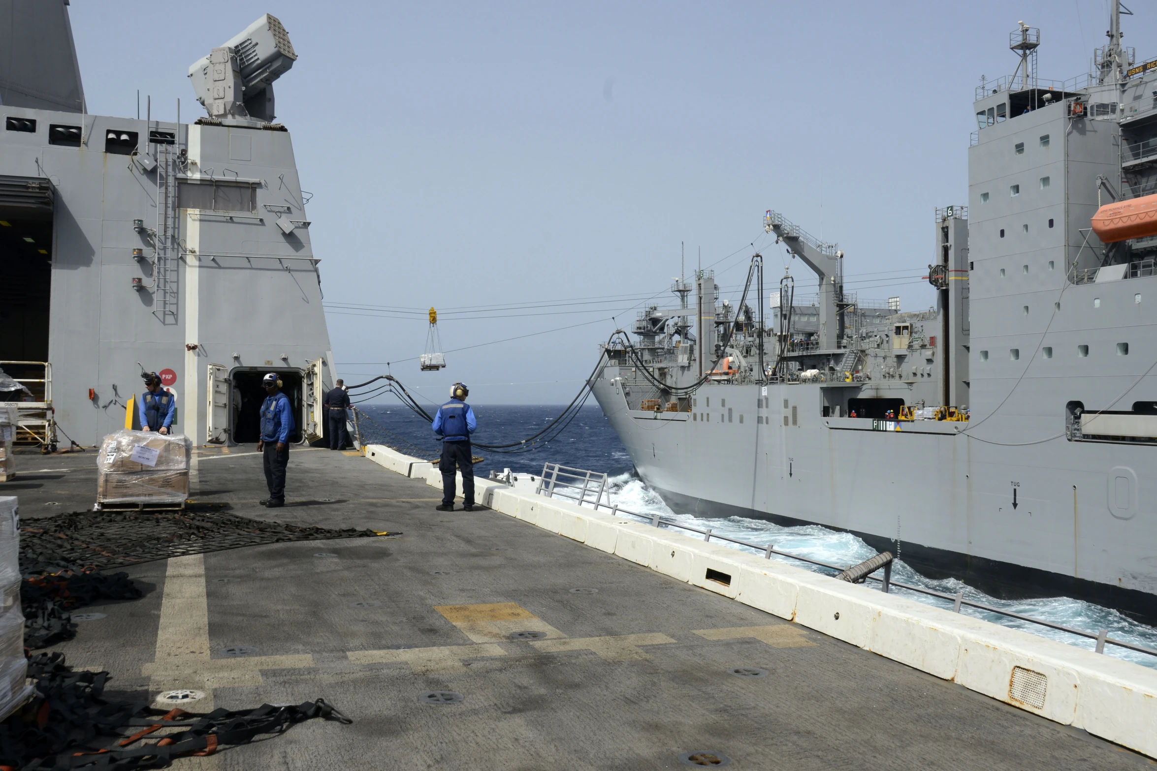 three navy people walk onto a boat near other military ships