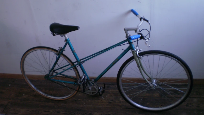 the blue bicycle is parked near the wall