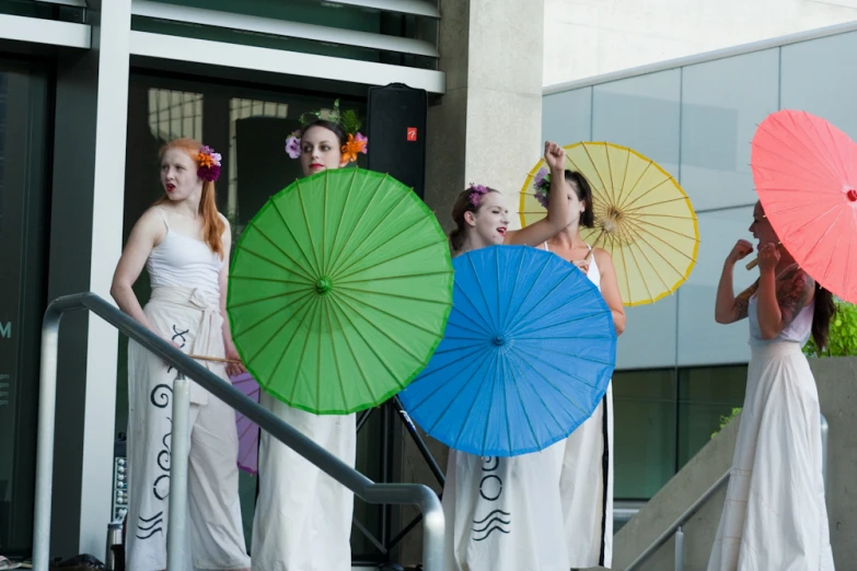 four women in white dresses holding umbrellas near stairs