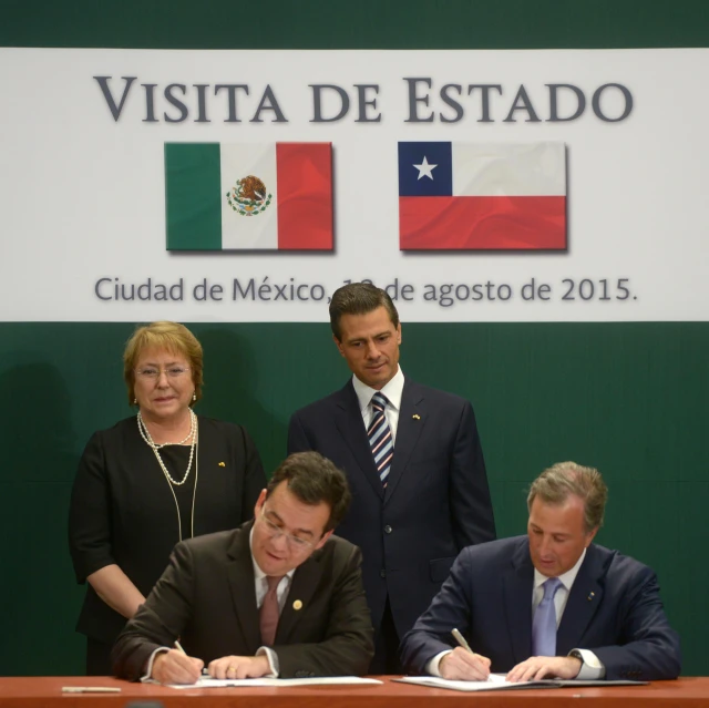 a man in a suit and tie sits at a table while holding a signed document