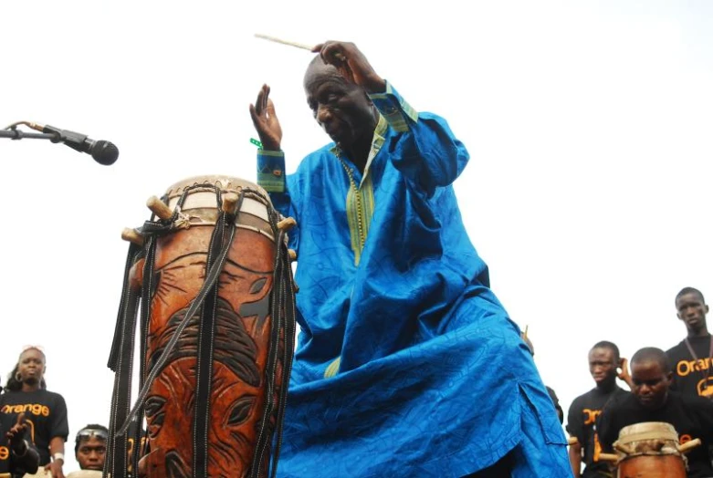 a group of men stand around a wooden instrument with one drum