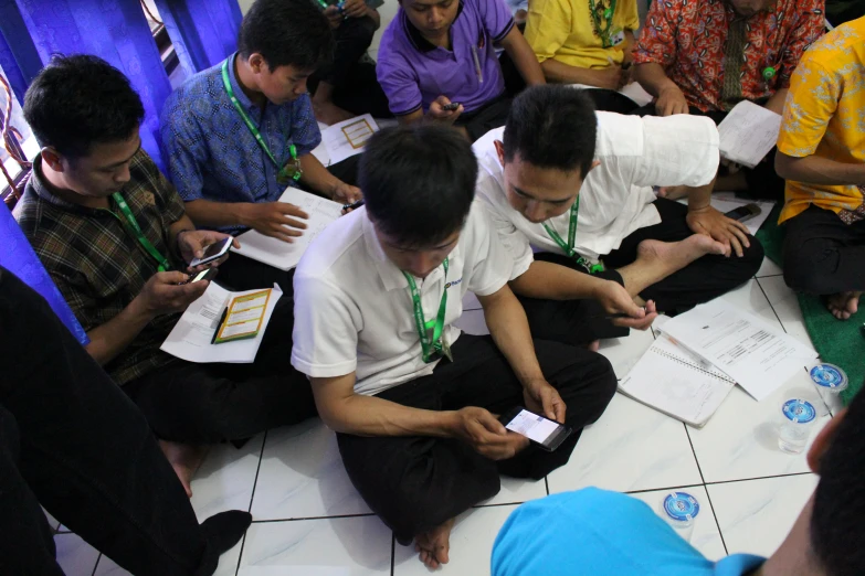 group of men sitting on the floor together using cellphones