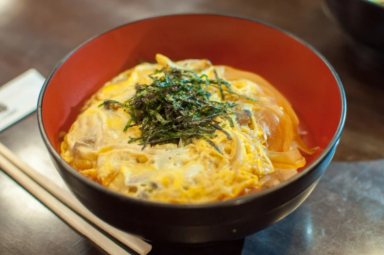 a red bowl filled with some food next to chop sticks