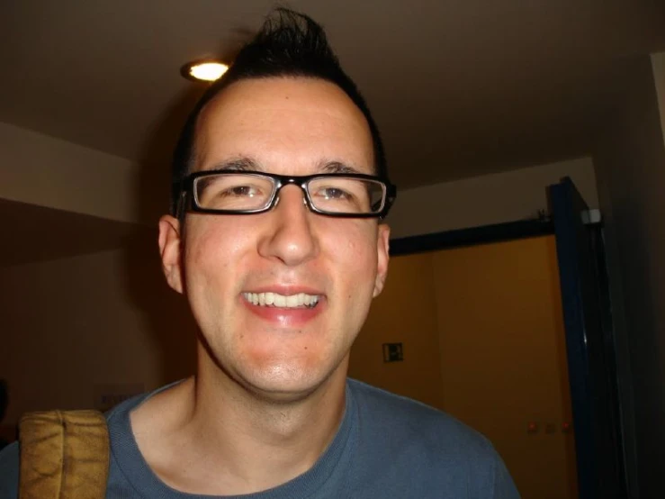 a man with glasses smiles as he is looking into the camera