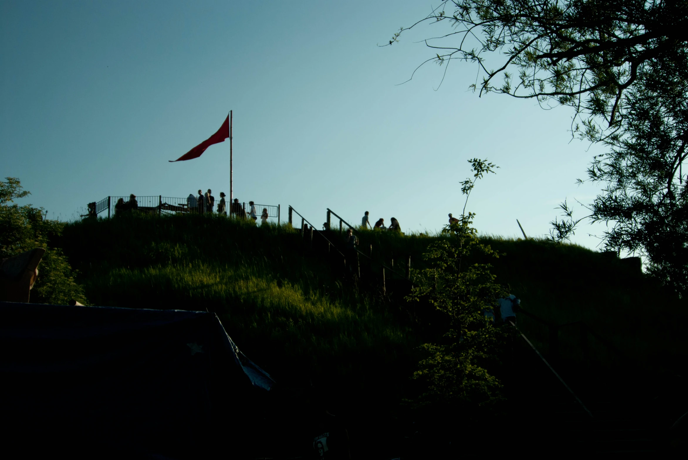 people stand on top of a hill while a red flag is flying