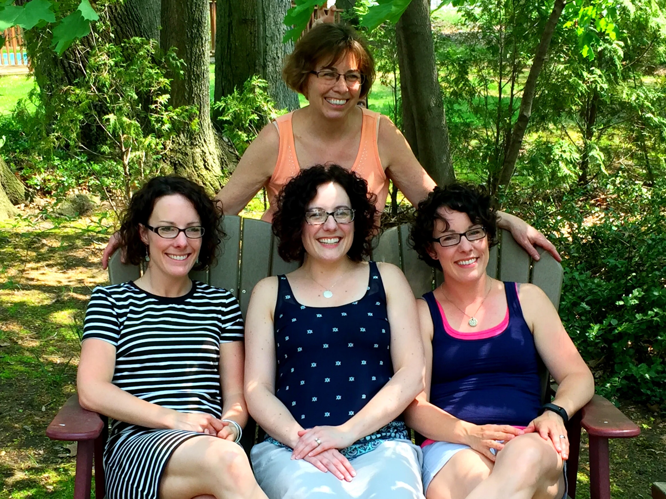 several smiling ladies are sitting on a bench in the park