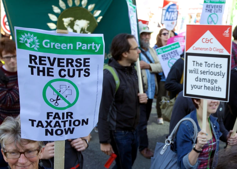 people gathered in the street, holding signs saying refuse the cuts