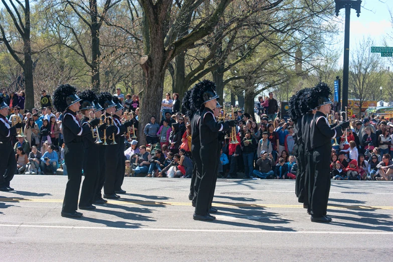 four uniformed people with marching gear standing on street in front of an audience