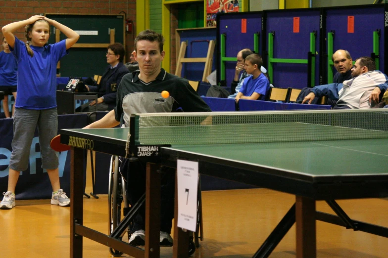 man holding racket in one hand and standing with a  sitting at the table looking off into the distance