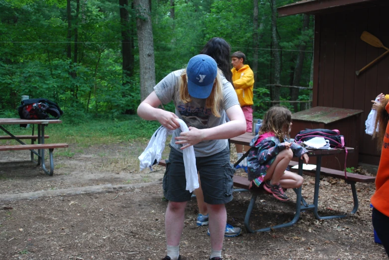 two girls wearing sun glasses and a blue hat picking up clothing from a picnic table