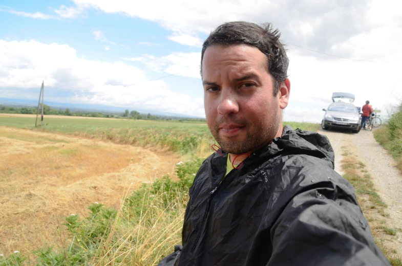 a man is posing in a field with cars behind him