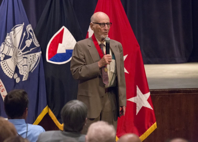 man speaking to a crowd while holding two flags