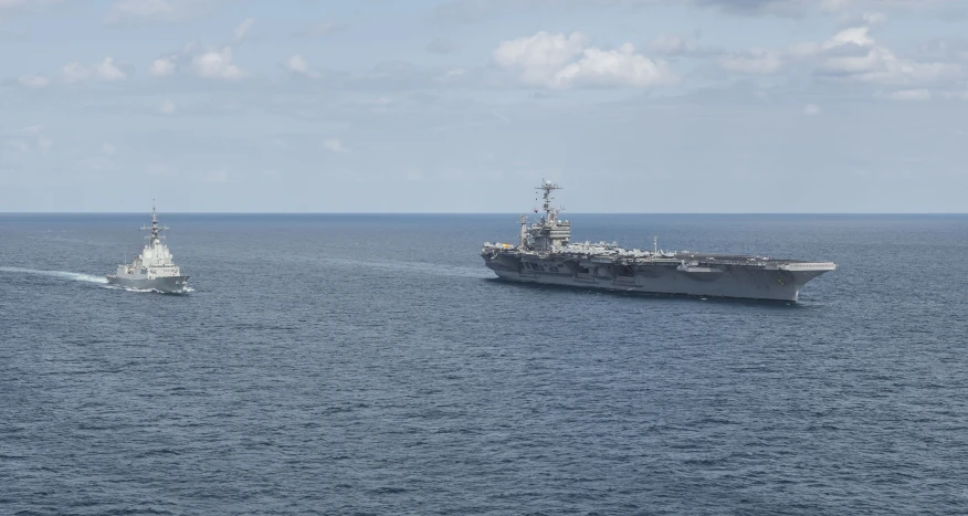 a large naval ship passing by another boat on the water