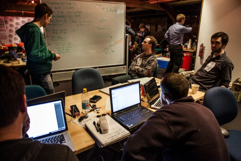 several people sit in front of a white board with laptop computers