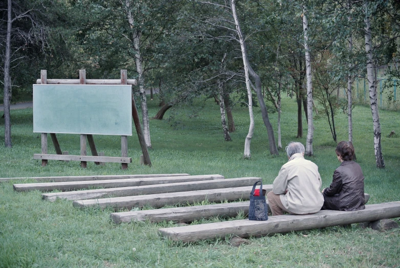 an old couple sitting on a bench watching a chalkboard