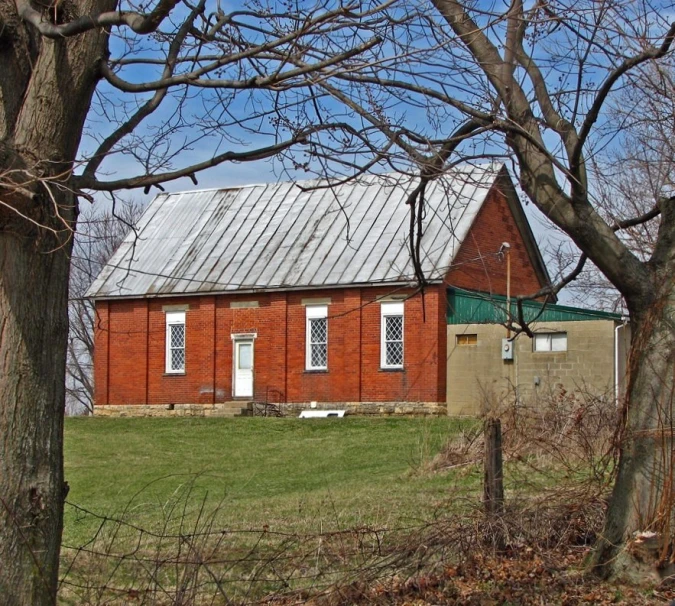 red brick building in rural country with fence, trees and grass