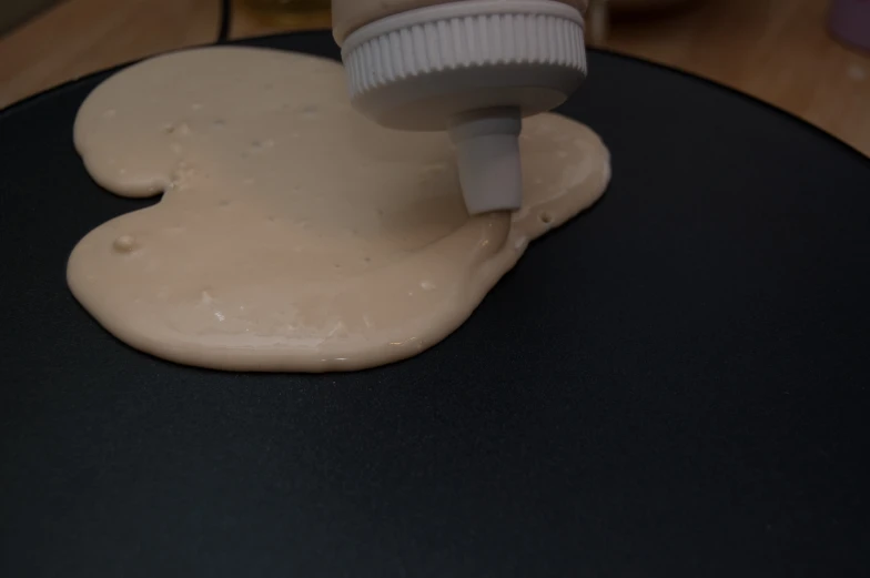 the bottle is pouring batter into the pan with white frosting